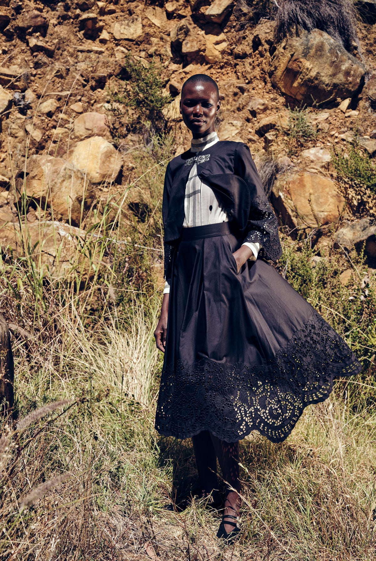 Person wearing a dark dress with lace details standing in a rocky, natural landscape. © stephane Gautronneau