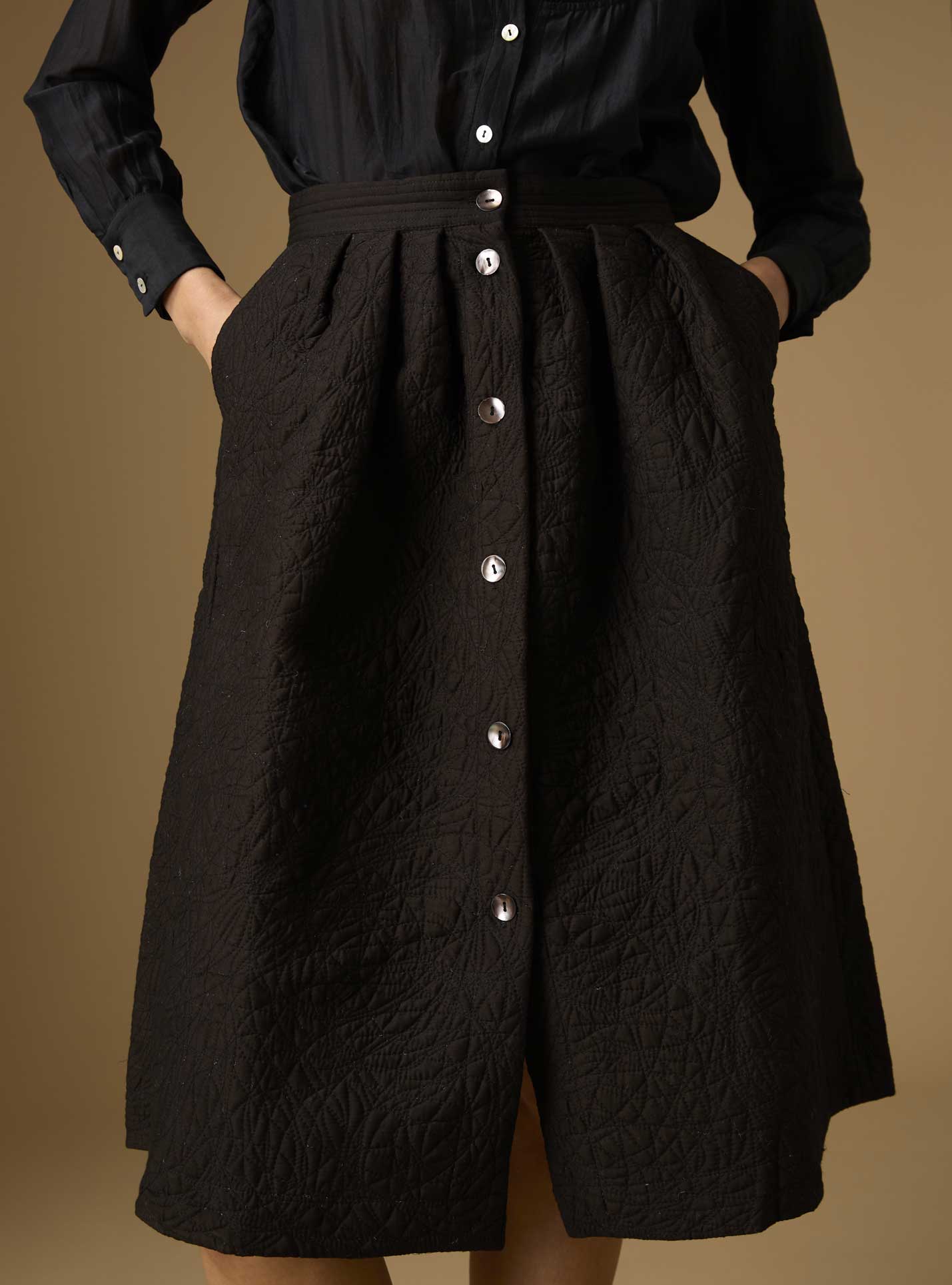 A black skirt with a buttoned front and quilted pattern, displayed on a mannequin.