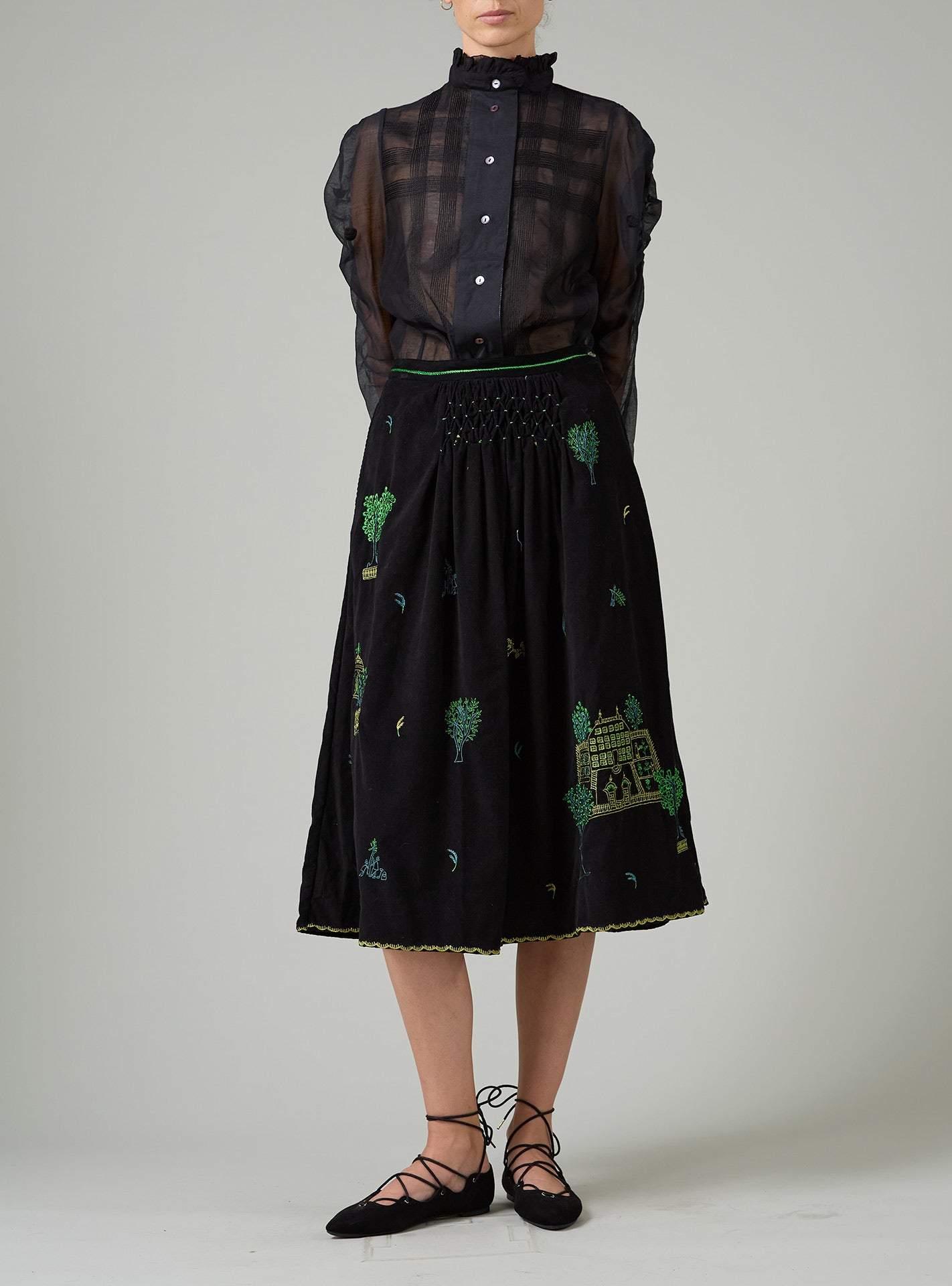 Black embroidered skirt with a black sheer blouse worn by a person on a plain background
