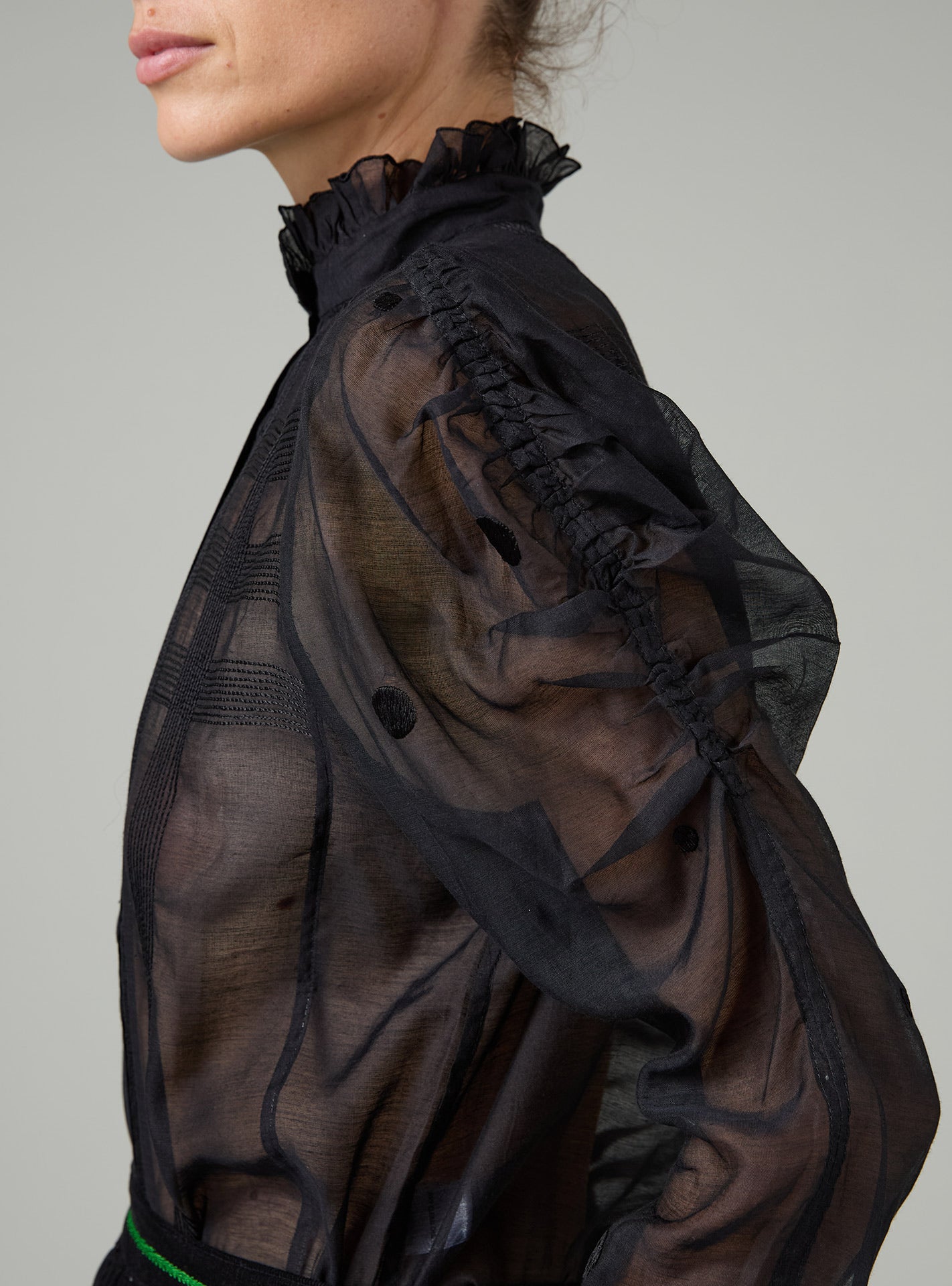 Black sheer blouse with ruffled details on a neutral background