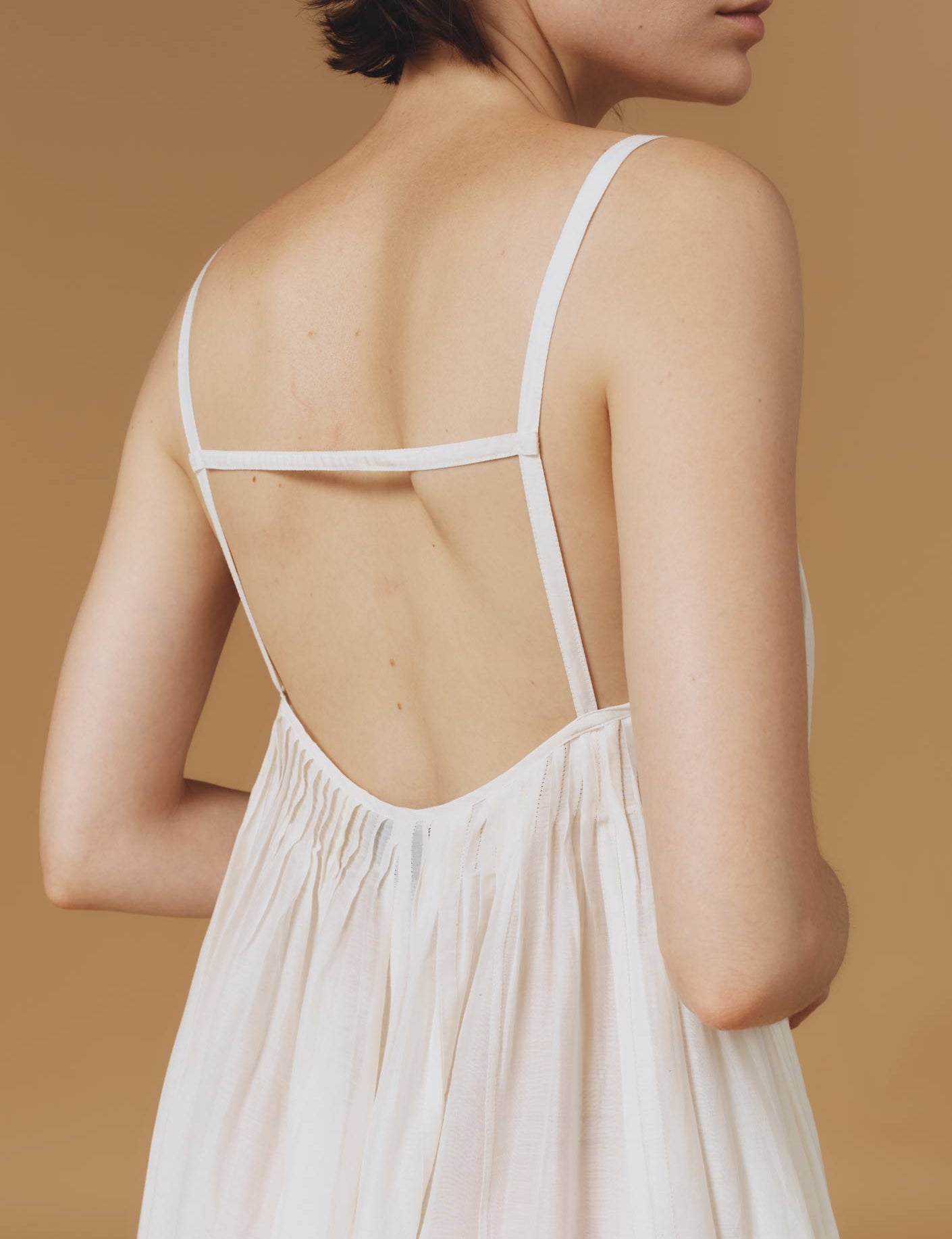 Close up back view of Zenobia Optical Pleats Off White long dress by Thierry Colson