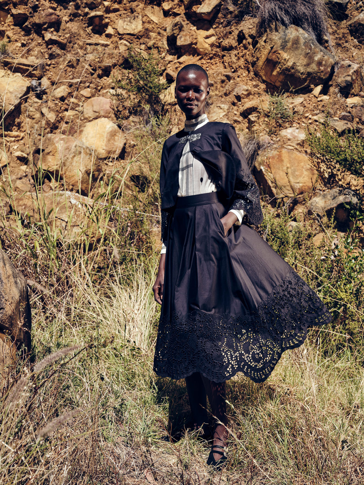 Person wearing a dark dress with lace details standing in a rocky, natural landscape. © stephane Gautronneau