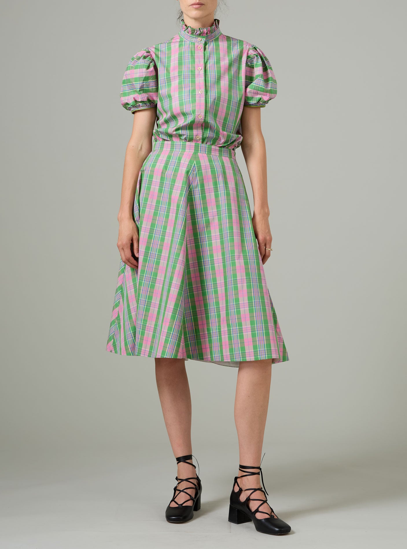 Person wearing a green and pink checkered skirt and blouse on a gray background
